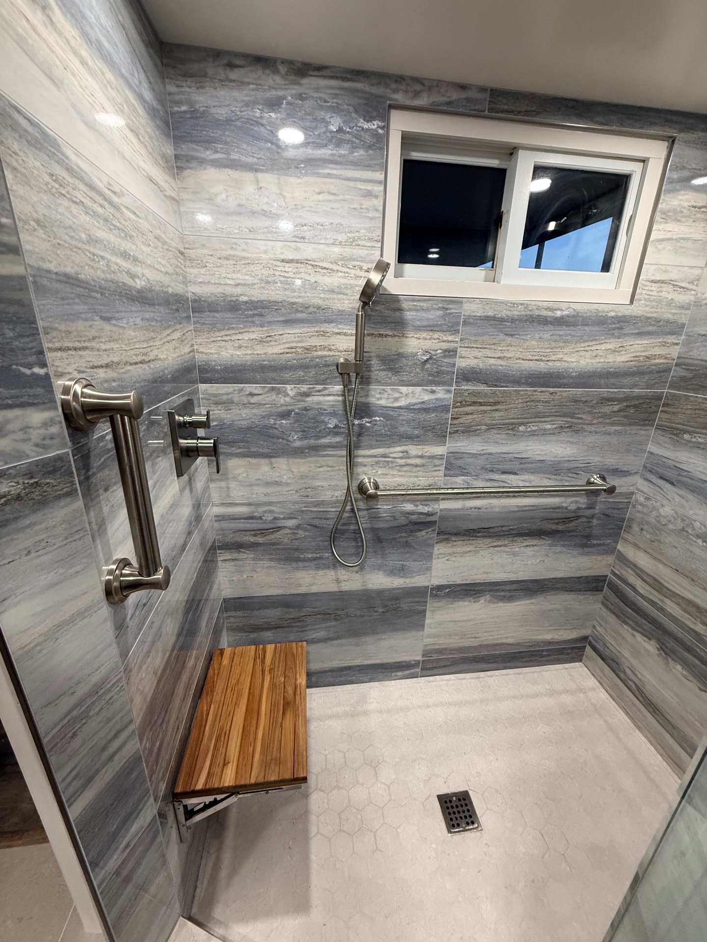 Custom walk-in shower remodel by MVW General Contractors featuring bookmatched marble tile, brushed nickel fixtures, and a teak folding bench